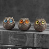 Trois statues de hiboux en résine faite à la main, avec plumes détaillées et yeux brillants, présentées sur une surface sombr