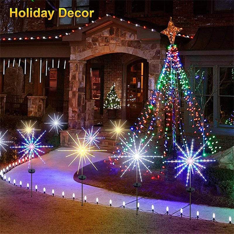 Outdoor holiday decor featuring a lighted Christmas tree and ground-level solar fireworks lights illuminating a pathway.