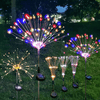 A display of bright, colorful solar fireworks lights shooting sparks into the night sky in a garden setting.
