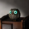 Statue de hibou en résine artisanale aux yeux bleus vifs sur un support en bois foncé.