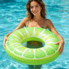 A woman floats in clear blue water holding a lime green fruit-themed inflatable pool float ring.