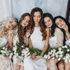 Six women with long brown hair wearing white dresses posing together