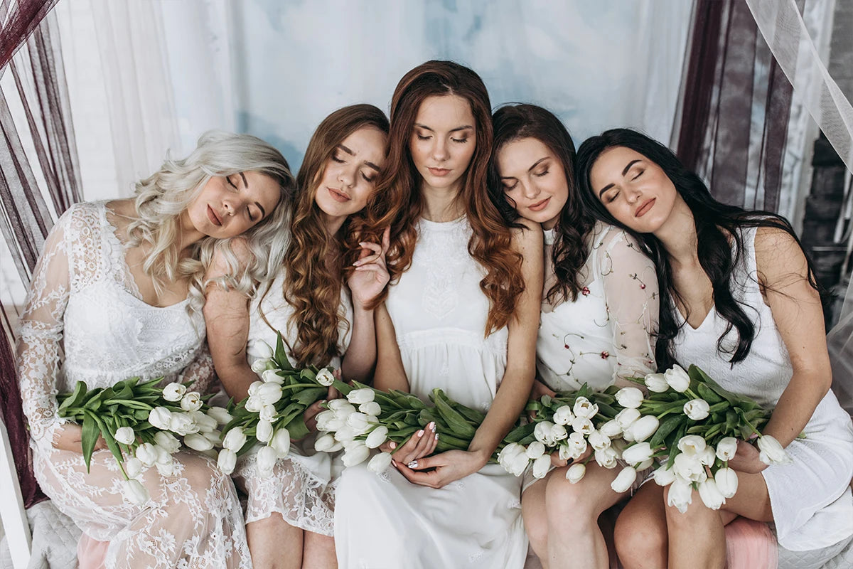 Six women with long brown hair wearing white dresses posing together