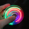 A hand holds a glowing, multi-colored LED fidget spinner with a kinetic gyroscope spinning on a dark surface.