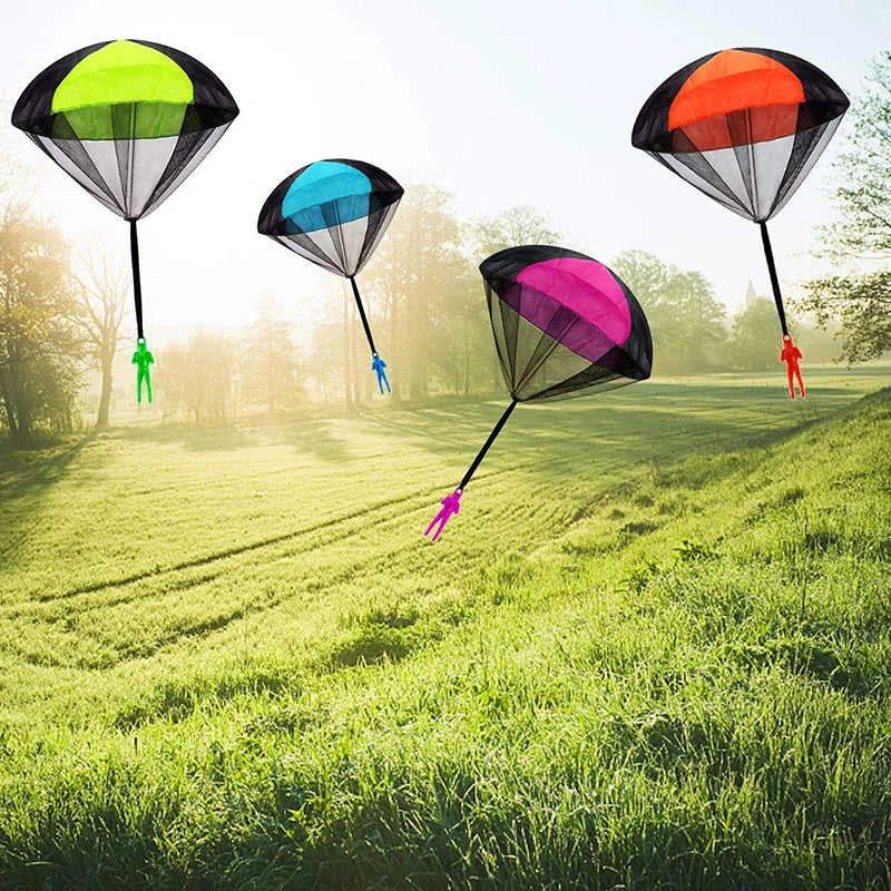Cinco juguetes paracaídas hechos a mano en varios colores vuelan sobre un campo de hierba bajo luz brillante.
