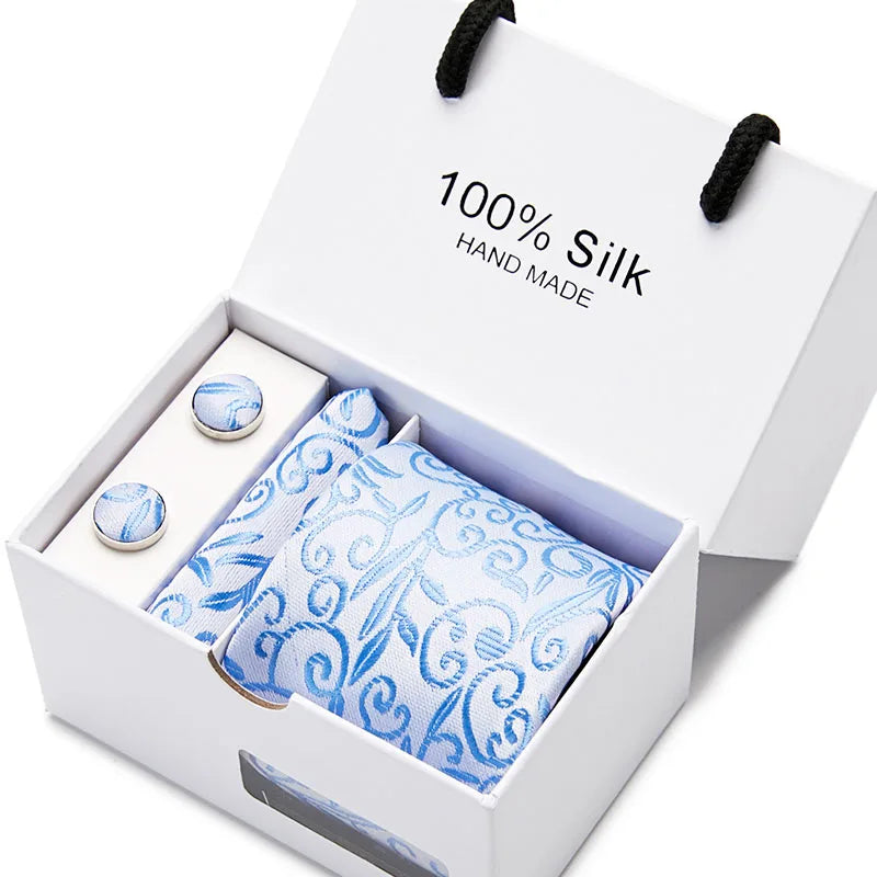 Caja blanca con corbata de seda azul marino estampada de cachemira hecha a mano y un pequeño accesorio redondo.