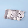 A set of nine baby socks in various gray, white, and striped patterns laid out on a light blue background.
