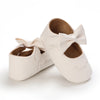 A pair of cream-colored soft non-slip baby first walker shoes with bow details.