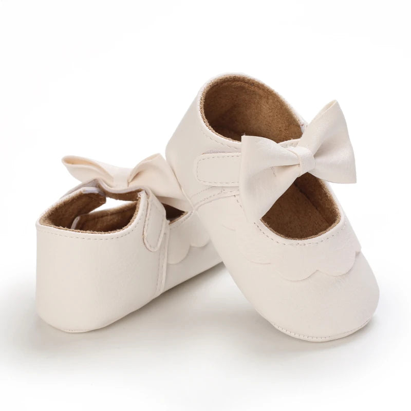 A pair of cream-colored soft non-slip baby first walker shoes with bow details.