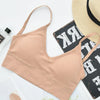 A beige seamless U-back bralette with thin straps is displayed next to a straw hat and a dark wooden surface.