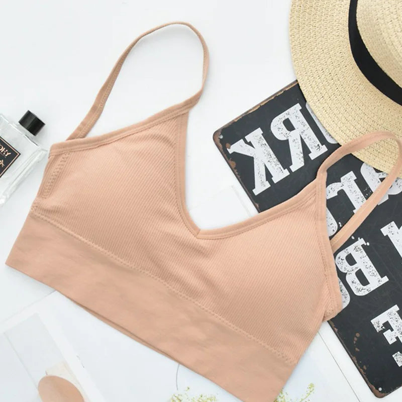 A beige seamless U-back bralette with thin straps is displayed next to a straw hat and a dark wooden surface.