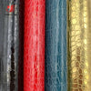 A vertical display of faux leather fabric rolls in various colors including black, red, blue, and gold crocodile pattern.