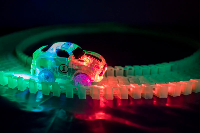 A small, glowing electric car is racing along a translucent magnetic track with ramps and bridges.