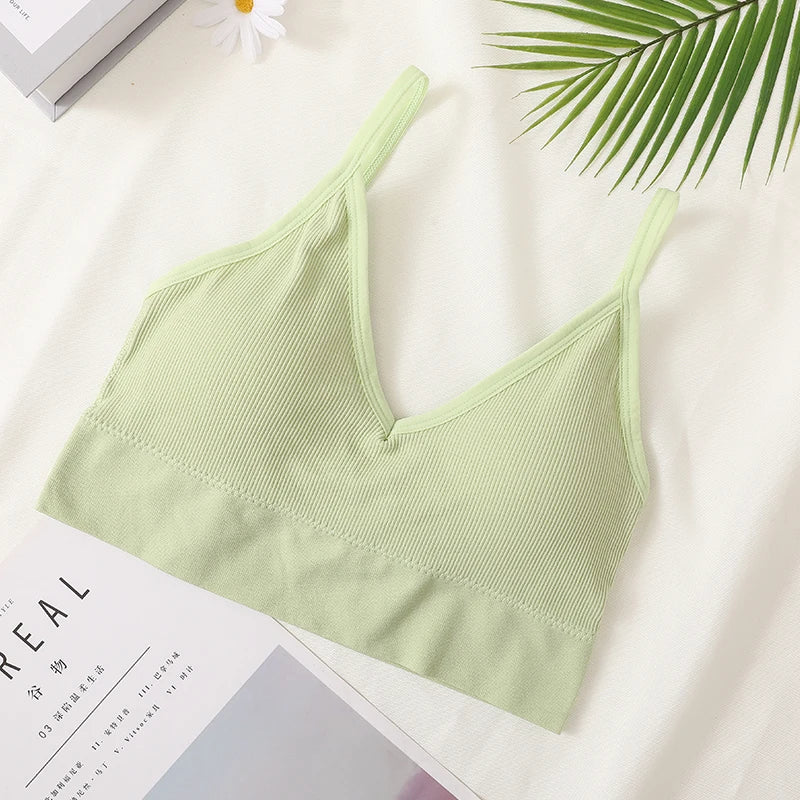 A light green seamless U-back bralette top displayed on a white background next to a green palm leaf.