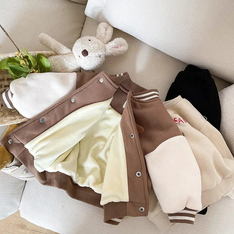 A brown corduroy jacket with cream lining is displayed on a light surface next to a stuffed animal.