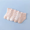 A set of five light pink and white patterned cotton baby socks laid out on a light blue background.