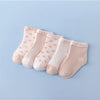 A set of five light pink and white patterned cotton baby socks laid out on a light blue background.