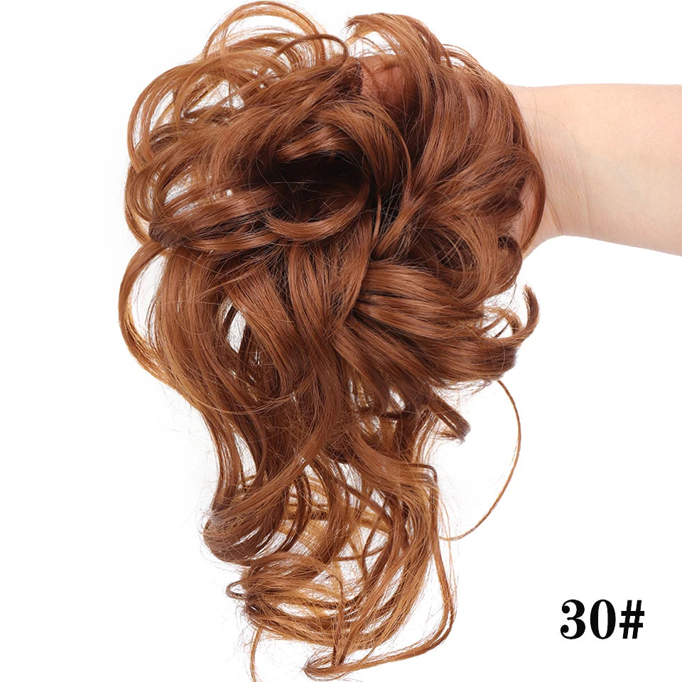 Una mano muestra un peinado rizado voluminoso y desordenado con cabello castaño rojizo recogido en un moño.