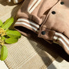 A close-up of a tan corduroy jacket with white stripes and black buttons lying on a woven mat.