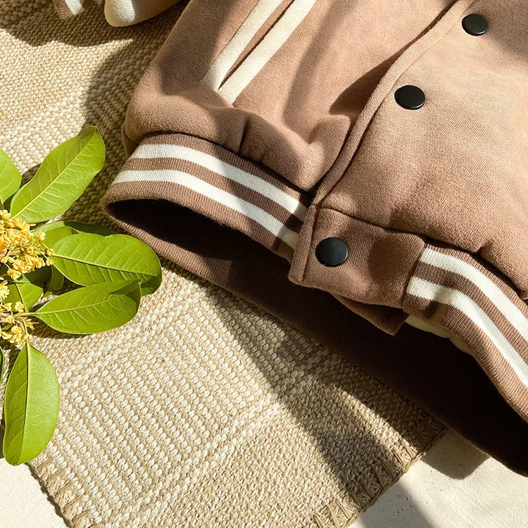 A close-up of a tan corduroy jacket with white stripes and black buttons lying on a woven mat.