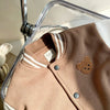 A tan corduroy jacket with white stripes and a small brown bear patch on the chest, displayed on a clear hanger.