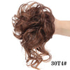 Primer plano de cabello rizado castaño rojizo recogido en un moño desordenado con una banda elástica.