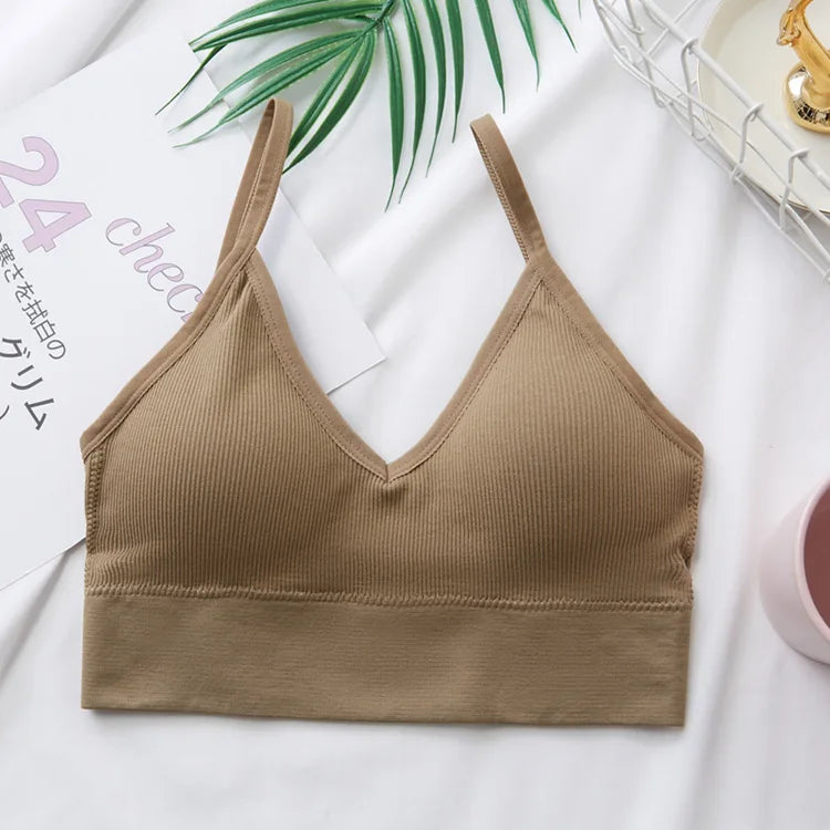 A beige seamless U-back bralette top is displayed on a white background next to a green palm leaf.