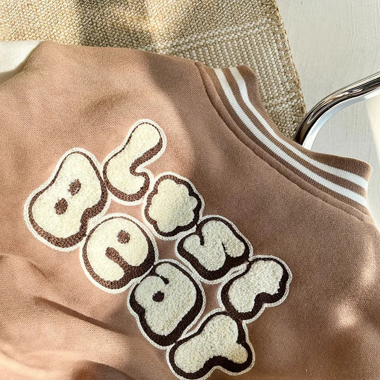 A close-up of a tan fleece jacket with embroidered beige lettering on the chest.