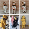A baby wearing a yellow winter down jacket and pants set with a faux fur hood standing outdoors.