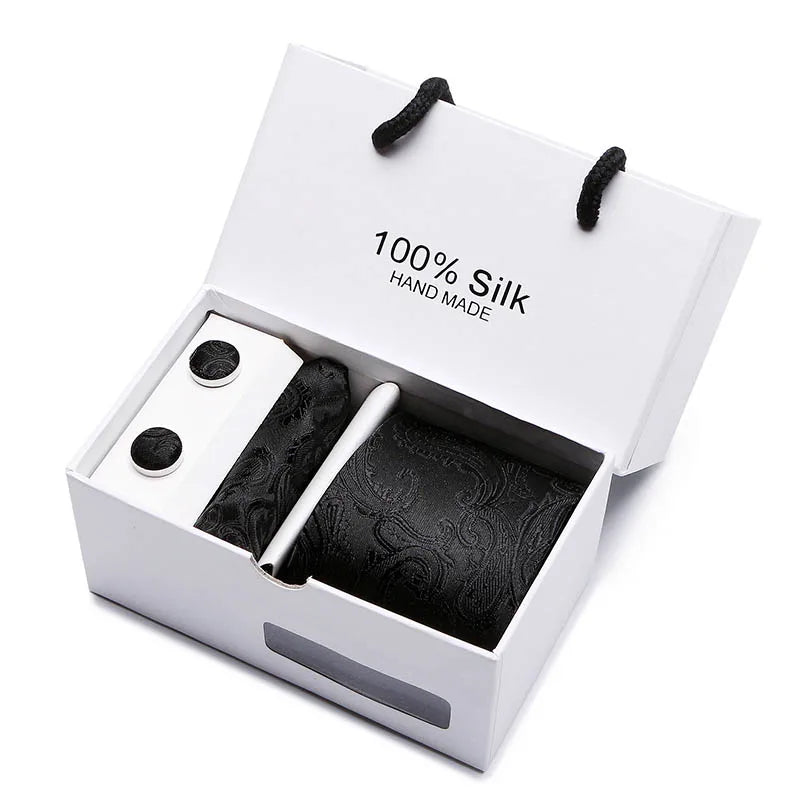 Una caja blanca con una corbata de seda jacquard azul marino con estampado de cachemir y corbatas negras.