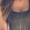 A close-up of a woman wearing a silver stick pendant bar necklace with a hollow geometric design.
