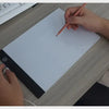 يد ترسم على لوح رسم LED أبيض مقاس A4 بقلم رصاص على مكتب خشبي