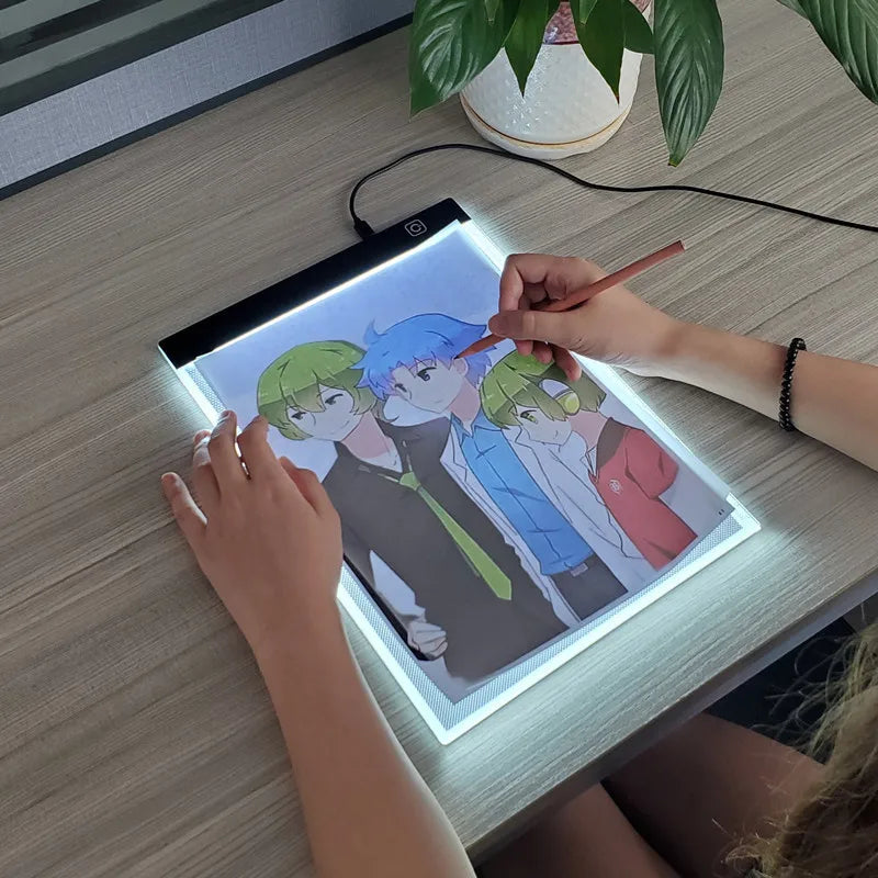 شخص يرسم على لوحة رسم LED مضاءة بحجم A4 باستخدام قلم على طاولة خشبية.