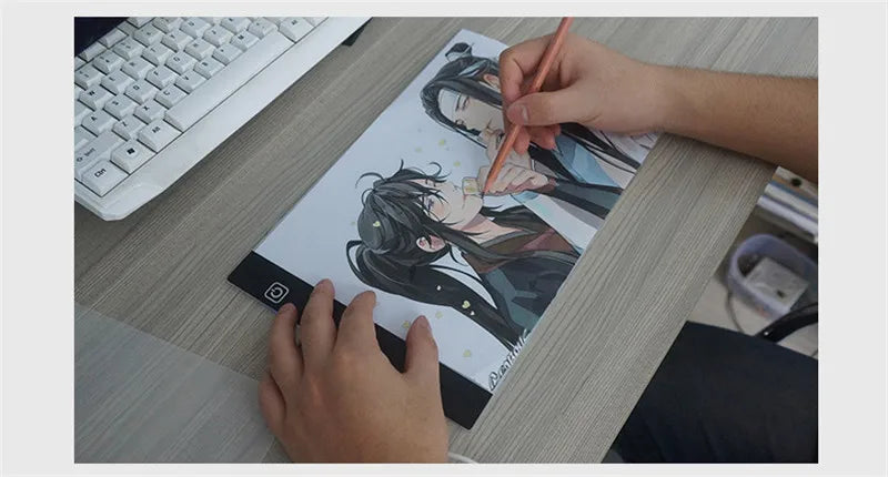 يد ترسم على لوحة رسم LED بحجم A4 بقلم ملون على طاولة خشبية.