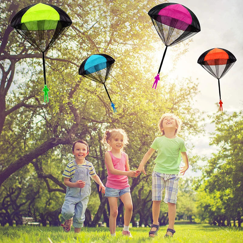 Tres juguetes de paracaídas coloridos sostenidos por niños en un parque soleado.
