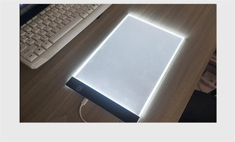لوحة رسم LED بيضاء مقاس A4 مع ضوء قابل للتعديل على مكتب خشبي بجانب لوحة مفاتيح