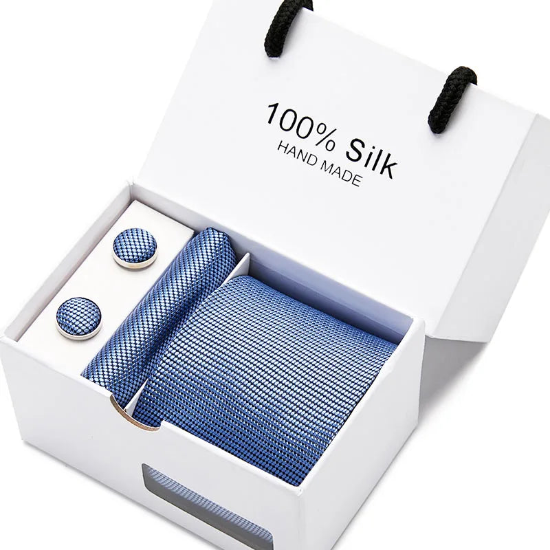 Una caja blanca con una corbata de seda azul marino hecha a mano, estampada con cachemir, y dos pequeños círculos de tela.
