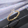 Nærbilde av en gull ring med rund cubic zirconia stein i en pave-fatning på mørk reflekterende overflate