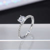 Nærbilde av klassisk rund bryllupsring med cubic zirconia og pavé-diamantband på hvit overflate.