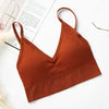 A terracotta orange seamless U-back bralette top is displayed on a white background next to some paper.