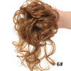 Una mano muestra un moño voluminoso y despeinado de cabello rizado con rizos sueltos y una banda elástica.