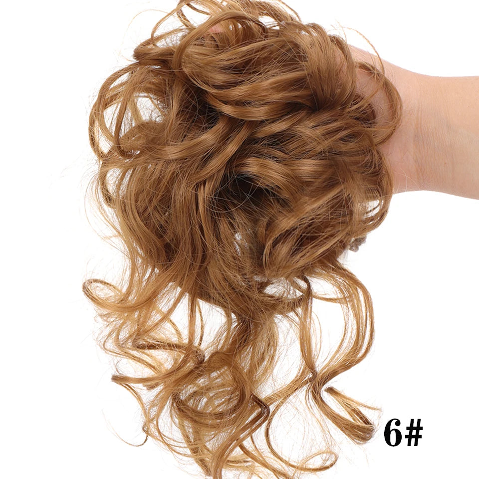 Una mano muestra un moño voluminoso y despeinado de cabello rizado con rizos sueltos y una banda elástica.