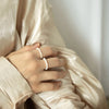En hånd med en håndlaget sterling sølv barokk perle justerbar ring, hvilende på drapert beige stoff.