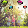 Tres coloridos juguetes paracaídas sostenidos por niños en un parque soleado.