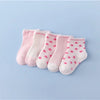 A set of pink baby socks with a white pattern laid out on a light blue background.