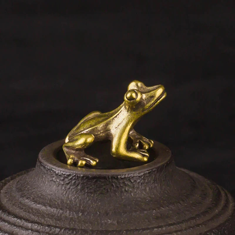 En miniatyrfigur av en vintage messingfrosk med gullfinish på en mørk, teksturert base.