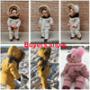 A baby wearing a yellow winter down jacket and pants set with a faux fur hood standing outdoors.