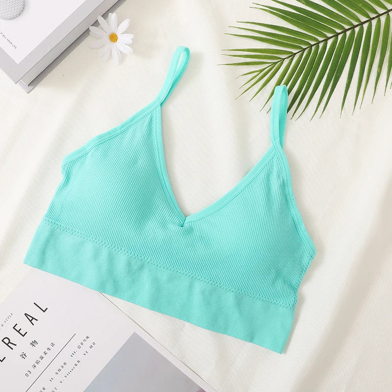 A light mint green seamless U-back bralette top displayed on a white surface next to a green palm leaf and a white flower.