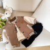 A brown corduroy jacket with cream sleeves and black pants is displayed on a light-colored surface.