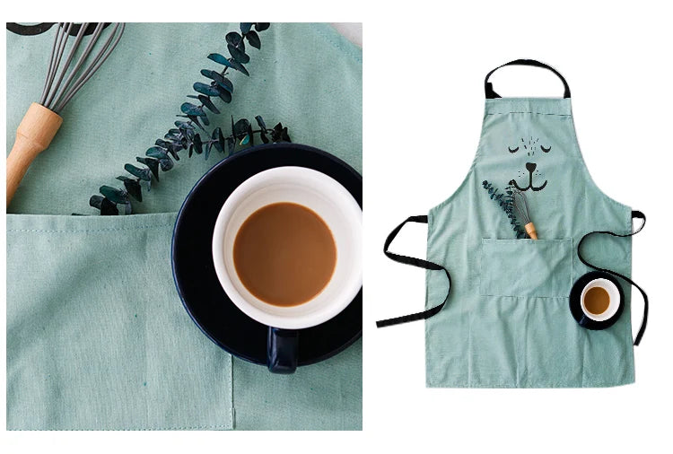 A light green cotton apron with a cartoon bear face and a small cup on a wooden surface.